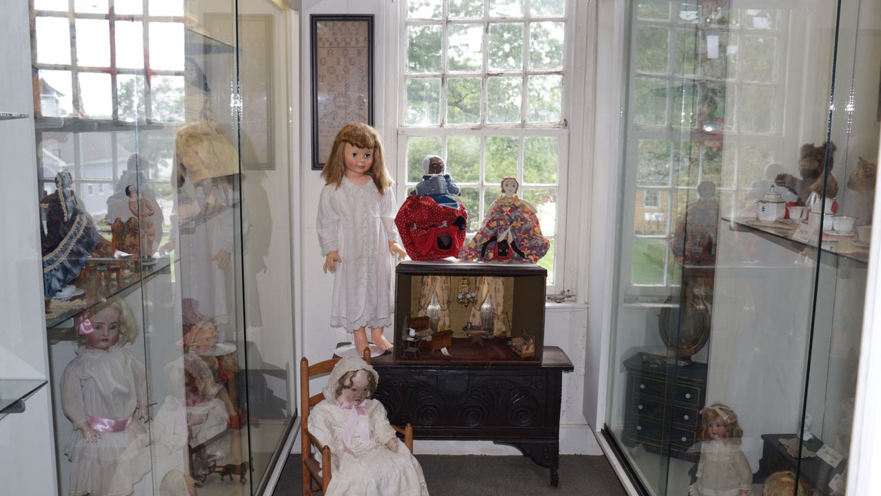Dolls displayed in glass cases and on an antique wooden chest.