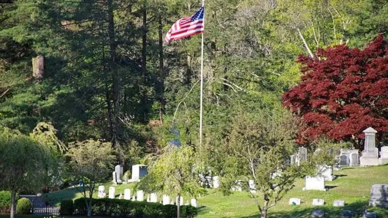 Gravestones and an American flag on a tree-lined hill at Lakeview Cemetery.