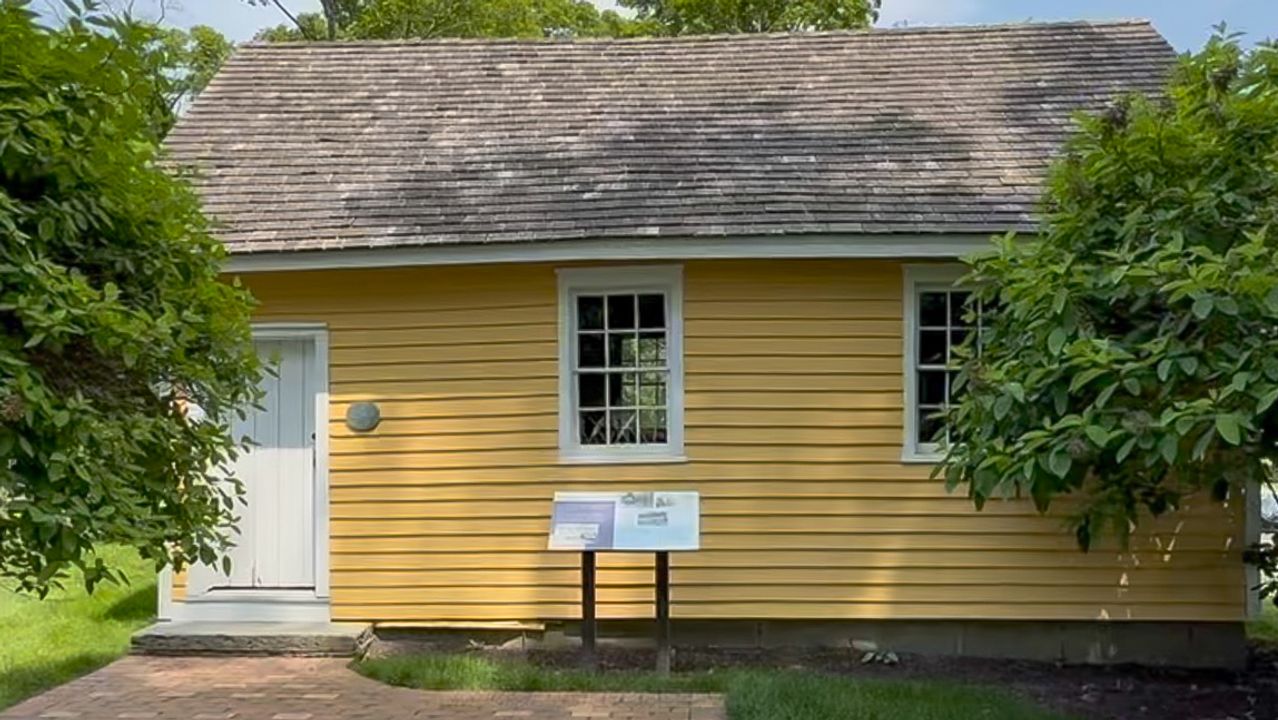 The yellow clapboard Rock School beside a brick path.